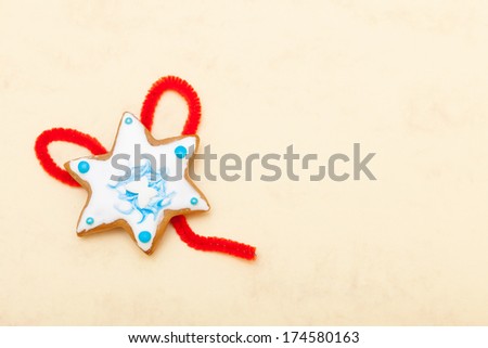 Homemade gingerbread cake star with icing and blue decoration and red string on brown paper background. Christmas and holiday handmade concept.