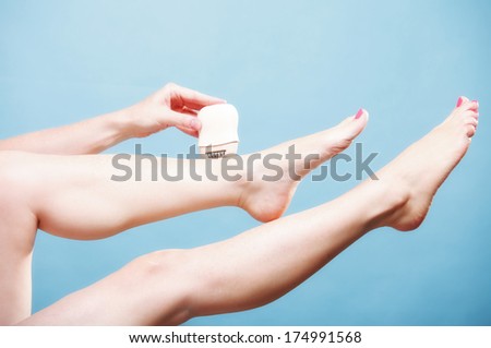 woman shaving her legs with electric shaver depilation on blue. Beauty and body skin care concept.
