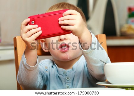 Funny dirty boy child kid taking photo with red mobile phone indoor. At home. Technology generation.