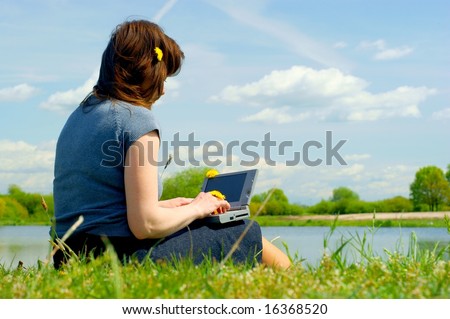 Woman typing on a laptop outside in a meadow. Blue sky with clouds. businesswoman notebook nature