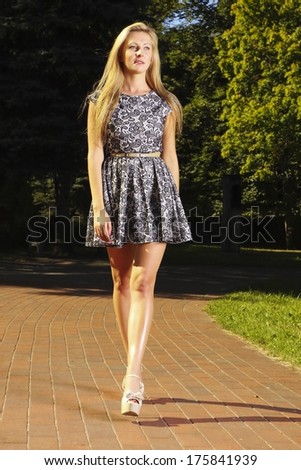 Full length fashionable young woman in summer flowery dress outdoor relaxing walking in park
