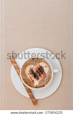White cup of hot beverage drink coffee cappuccino latte with heart love symbol froth and sweet waffle roll stick with cream on brown background. Studio shot.