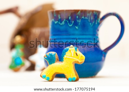 Blue mug of hot beverage drink tea or coffee and homemade gingerbread cake pony with icing and blue yellow decoration. Christmas and holiday handmade concept.