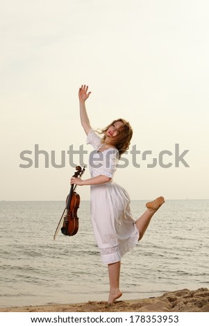 The blonde girl music lover on beach with a violin at sunset or sunrise.  Love of music concept.