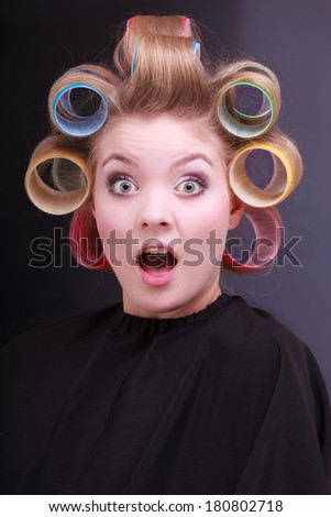 Portrait of funny surprised woman in beauty salon. Shocked blond girl with hair curlers rollers by hairdresser. Hairstyle.