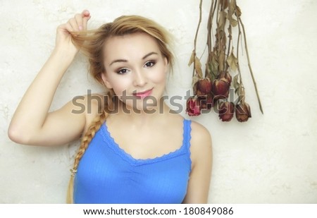 Hair problem. Blond woman teenage girl showing her damaged dry hair standing by bunch of dried roses flowers. Indoor.