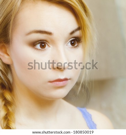 Candid portrait of pensive young woman with blond braided hair. Face of thoughtful teenage girl. Indoor.