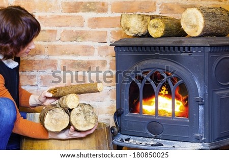 Winter at home. Woman putting some more wood on fire fireplace. Heating.