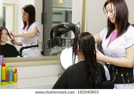 Reflection in mirror. Hairstylist hairdresser combing hair of female client. Woman in hairdressing beauty salon.
