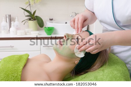 Beauty treatment concept. Woman relaxing in spa salon. Cosmetician removing clay facial mask from female face. Body care healthy lifestyle.