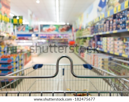 View from shopping cart trolley basket at supermarket self-service grocery shop. Retail. Blurred background.