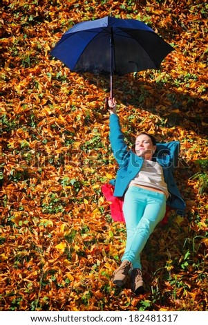 Fall lifestyle concept. Casual young woman girl relaxing with blue umbrella in autumnal park. Golden colorful leaves background