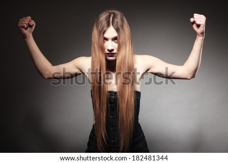 Sad young woman with long hair and creative makeup. Unhappy girl showing her muscles power in dark. Negative emotions. Studio shot.