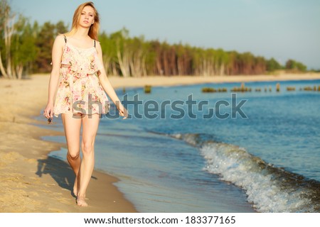 Vacation. Girl in summer dress walking alone on the empty beach. Young woman relaxing on the sea coast. Summertime.