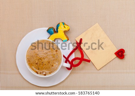 White cup of hot beverage drink coffee cappuccino latte with christmas handmade gingerbread cake pony dessert and blank paper card space for text message with red heart symbol love. Holiday concept.