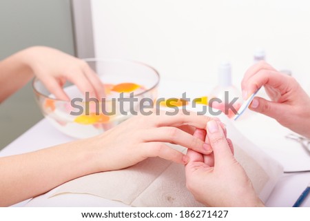 Beautician with file filing nails female client. Woman spa beauty salon