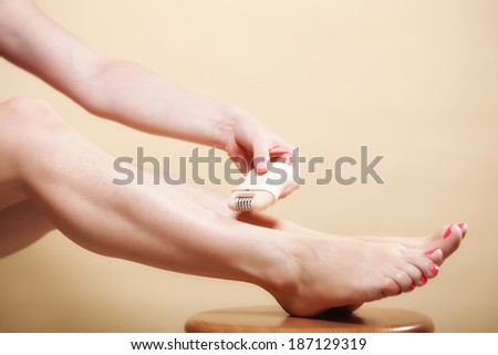 woman shaving her legs with electric shaver depilation on orange. Beauty and skin body care concept.