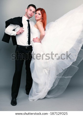 Wedding day. Portrait of happy married couple red haired bride and groom in full length studio shot on gray background