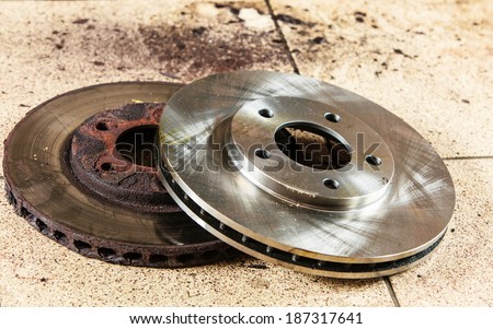 Auto in service. New and old front brake disks for modern car lying on floor in mechanic garage car service.