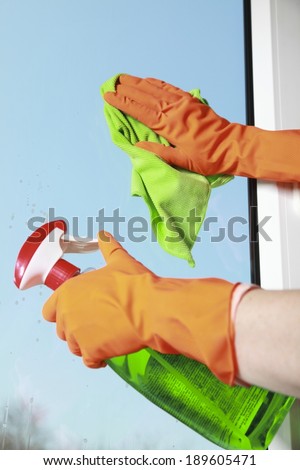 hand in orange glove cleaning window with green rag and spray detergent. Spring cleaning concept