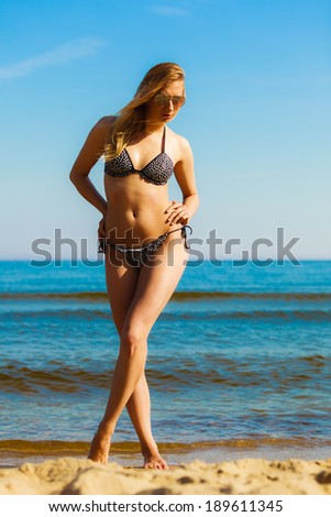 Vacation. Sexy girl in bikini standing alone on the empty beach. Young woman relaxing on the sea coast. Summertime.