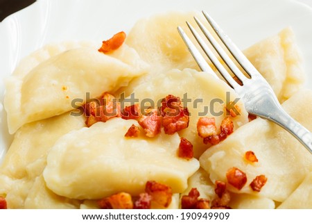 Closeup of dumplings sprinkled with pork scratchings with fork as food background. Traditional polish (Poland) cuisine.