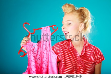 Pinup blond girl young woman in retro style buying clothes. Client customer holding pink dress on vibrant blue. Retail and sale. Studio shot.
