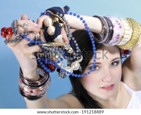 young woman in summer style with plenty of jewellery, beads in hands blue background