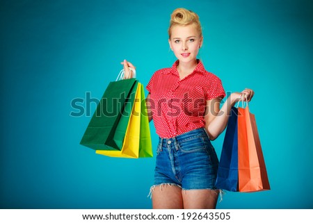 Pinup girl young woman in retro style buying clothes. Client holding colorful shopping bags on vibrant blue. Retail and sale. Studio shot.