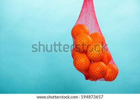 Mesh bag of fresh oranges healthy tropical fruits from supermarket on blue. Food retail.