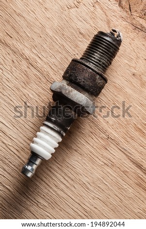 Auto service. Old rusty spark plug as spare part of car transportation on wooden background.