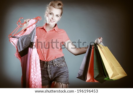 Pinup girl young woman in retro style buying clothes. Client holding shopping bags and pink dress on gray. Retail and sale. Studio shot.