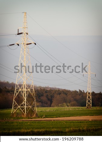 Energy. High voltage post. Electricity pylons power lines high-voltage towers on green field.