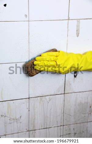 gloved hand cleaning dirty old tiles with brush in a bathroom