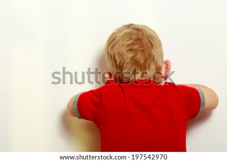 Happy childhood. Back view. Blond boy child covering his face. Kid preschooler playing hide-and-seek or blind man\'s buff. Indoor.