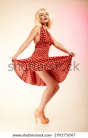 Vintage pinup style. Full length of stylish woman dancing. Girl in blond wig and retro spotted red dress on pink. Disguise. Party.
