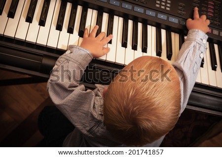 Happy childhood and music. Little boy child kid playing on the black digital midi keyboard piano synthesizer musical instrument indoor.