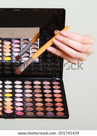 Closeup of colorful eyeshadows palette with mirror and makeup brush in female hand of stylist. Cosmetology.