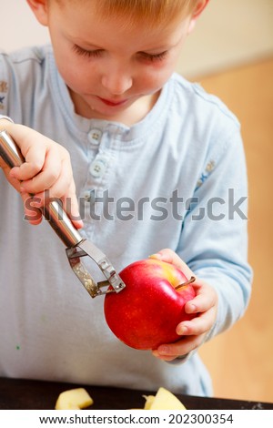 Blond boy child kid preschooler peelings fruit apple at home. Happy childhood.