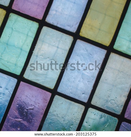 multicolored stained glass window with regular block pattern in hue of blue green violet, square format