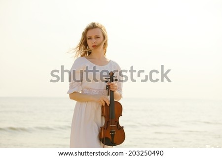 The blonde girl music lover on beach with a violin at sunset or sunrise.  Love of music concept.