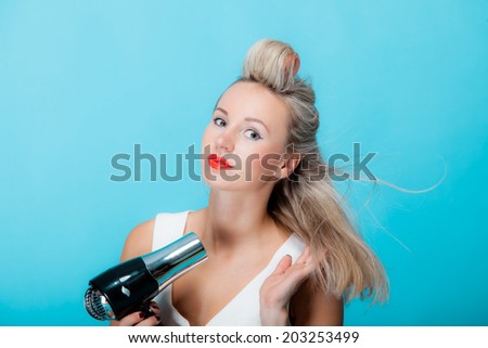 young woman preparing to party, sexy girl fashion model styling hair with curlers accessories and hairdreyer retro style vivid blue background