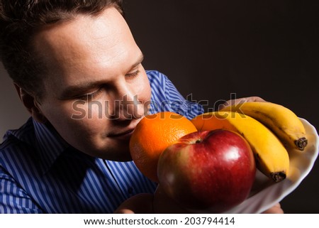 Diet and nutrition. Happy young man smelling fruits on dark gray. Guy recommending healthy nutrition.