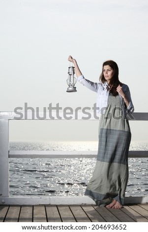 Full length young woman on pier with a oil kerosene lamp. Concept carrying light, daylight