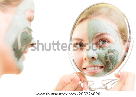 Skin care. Woman in clay mud mask on face with heart symbol of love on cheek looking in the mirror. Girl taking care of dry complexion.
