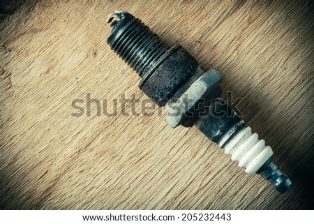 Auto service. Old rusty spark plug as spare part of car transportation on wooden background.