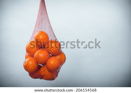 Mesh bag of fresh oranges healthy tropical fruits from supermarket on gray. Food retail.