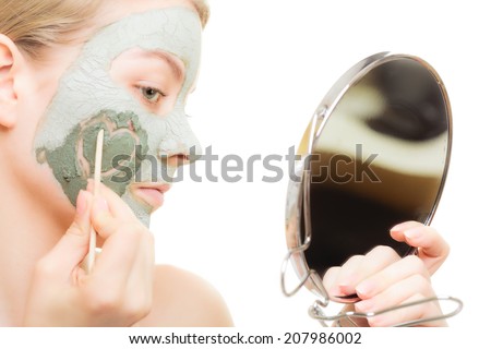 Skin care. Woman in clay mud mask on face looking in the mirror. Girl taking care of dry complexion drawing heart on cheek.