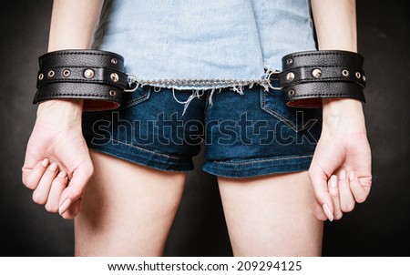 Arrest and jail. Closeup of leather handcuffs on hands of criminal woman prisoner girl on gray. Punishment.
