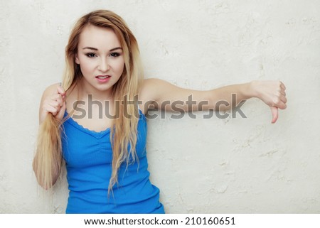 Hair problem. Blond woman teenage girl holding her damaged dry hair showing thumb down hand sign gesture. Indoor.